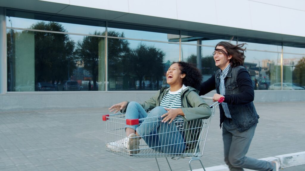Two people riding in a shopping cart outside.