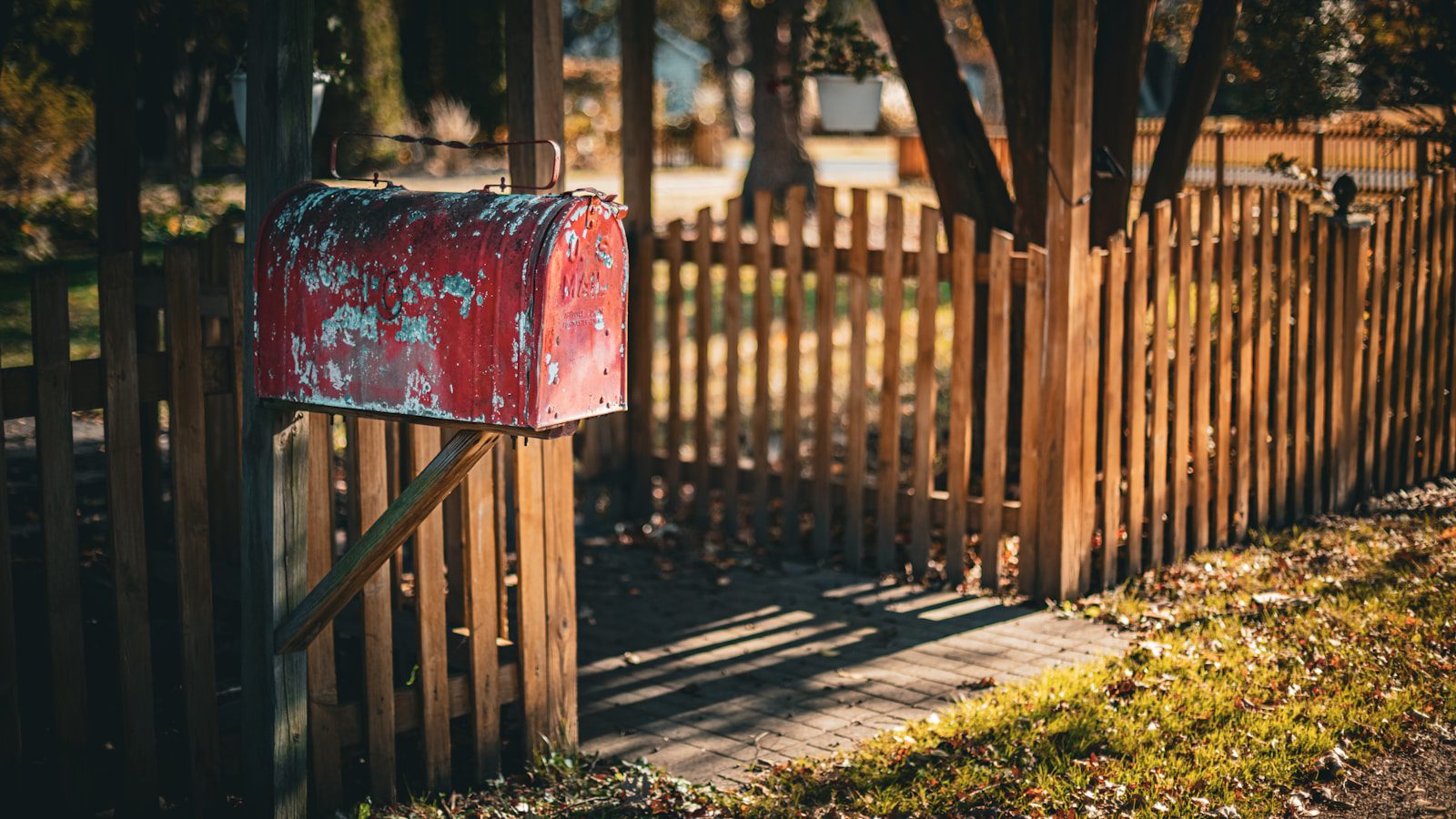 A weathered red mailbox stands by a wooden fence.