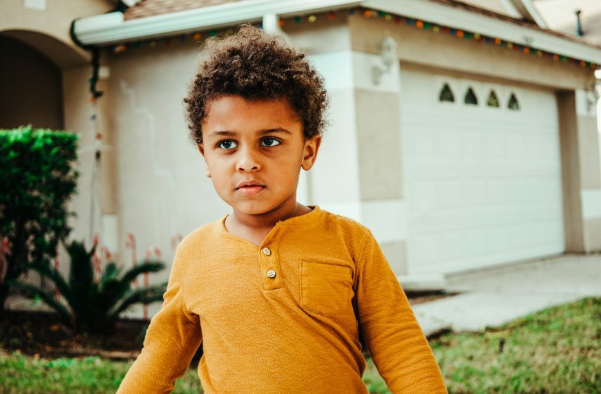 boy in yellow henley long sleeve shirt standing near white building during daytime