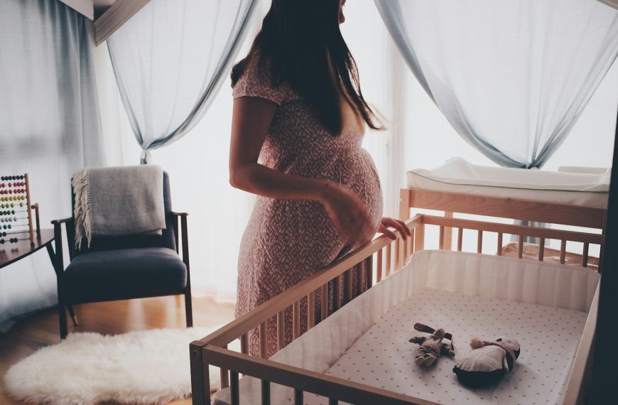 woman in white lace sleeveless dress standing beside brown wooden crib