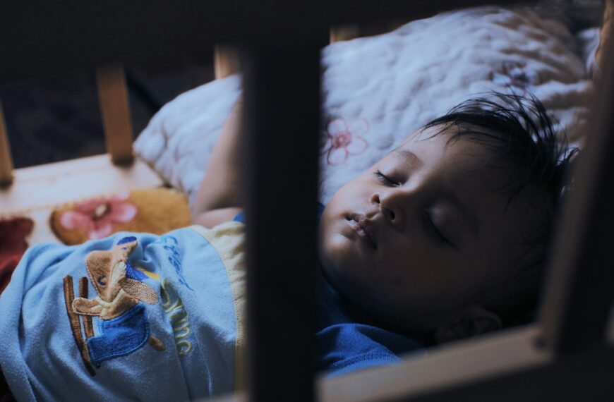 a young child sleeping in a crib with a stuffed animal