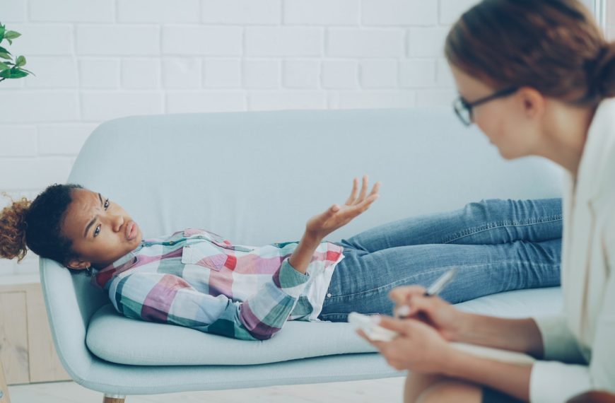 Therapist listens to young woman on couch.