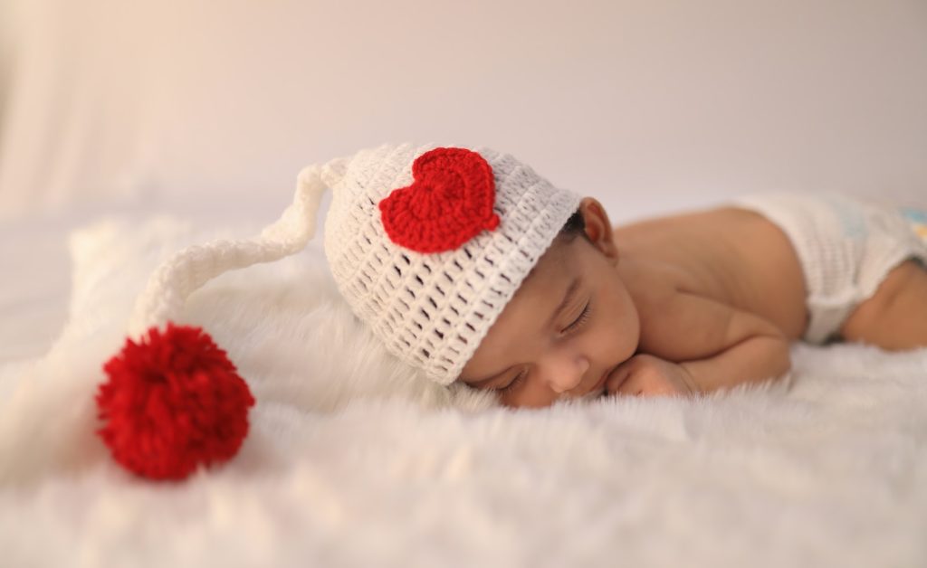 baby in white knit cap lying on white textile