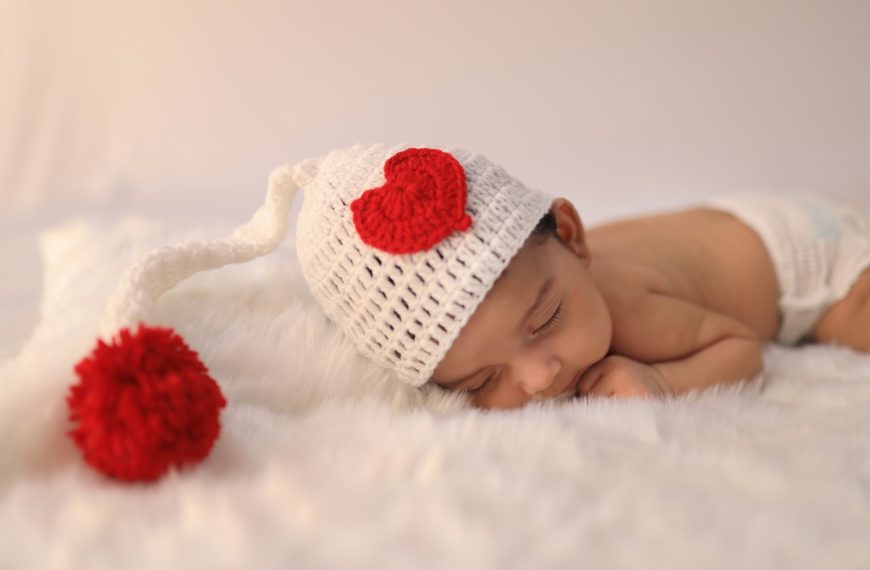 baby in white knit cap lying on white textile