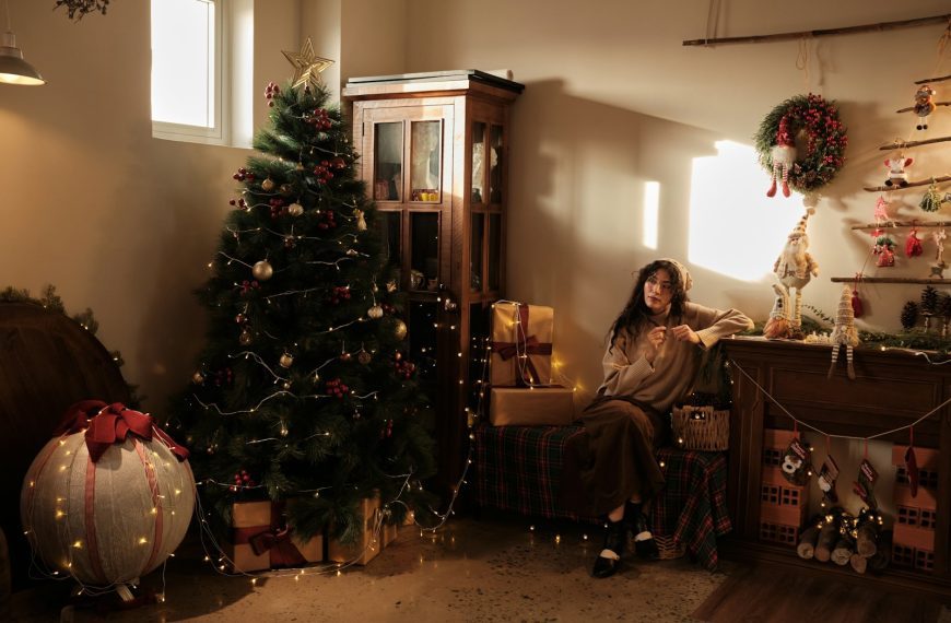 Woman sitting by a decorated christmas tree and gifts.