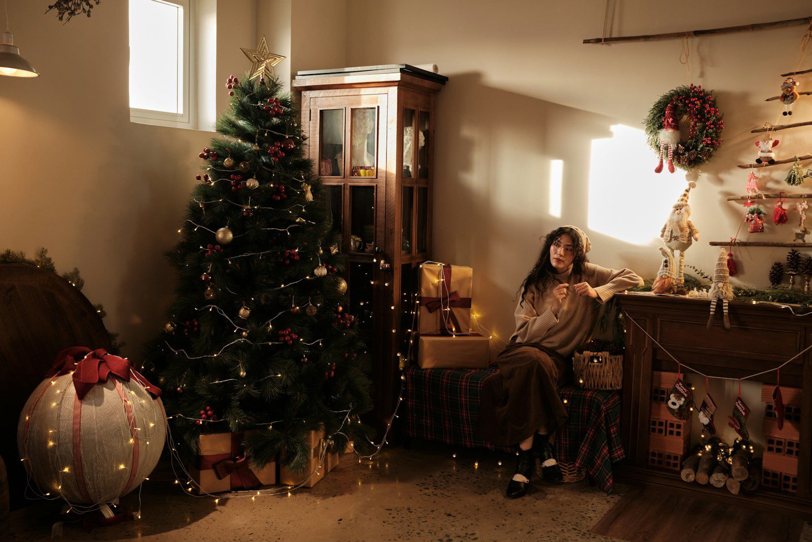 Woman sitting by a decorated christmas tree and gifts.