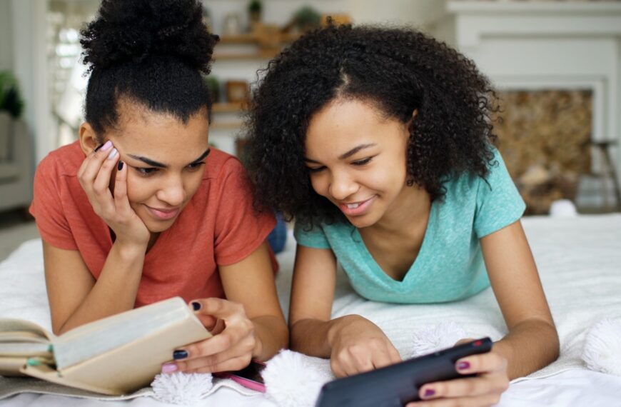 Two young women looking at a phone and book.