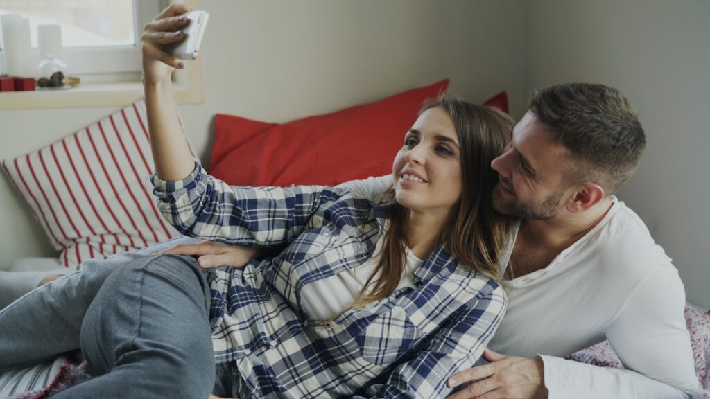 Couple taking a selfie while lying on a bed.