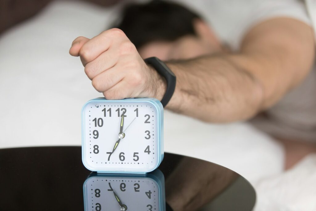 A man laying in bed with a clock on top of him