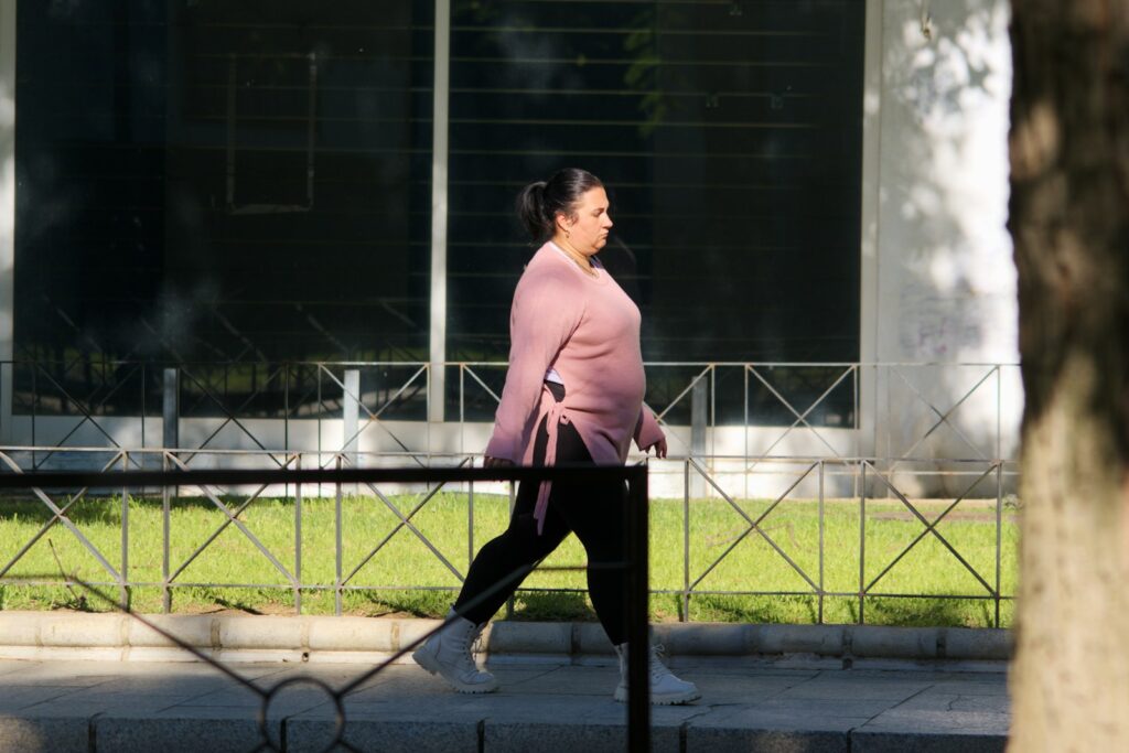 A woman walks along a sidewalk next to a fence.