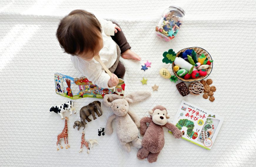 boy sitting on white cloth surrounded by toys