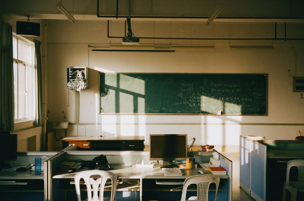 Sunlight streams into an empty classroom with desks.