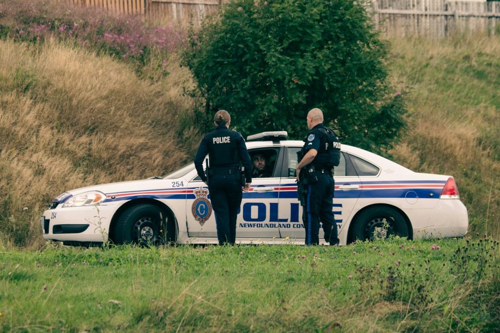 2 men standing beside white and blue police car