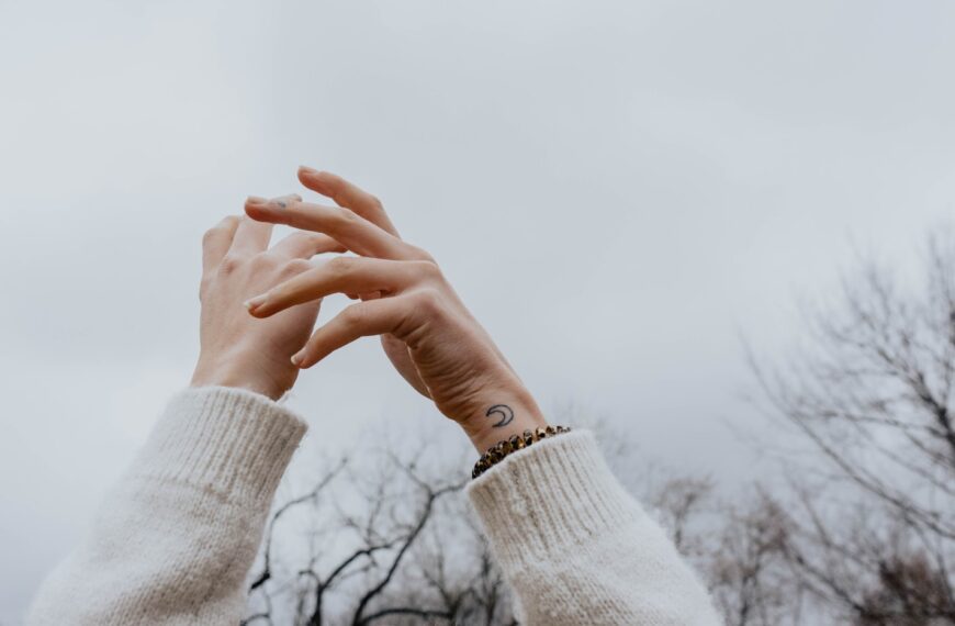 person wearing white sweater raising hands under white sky