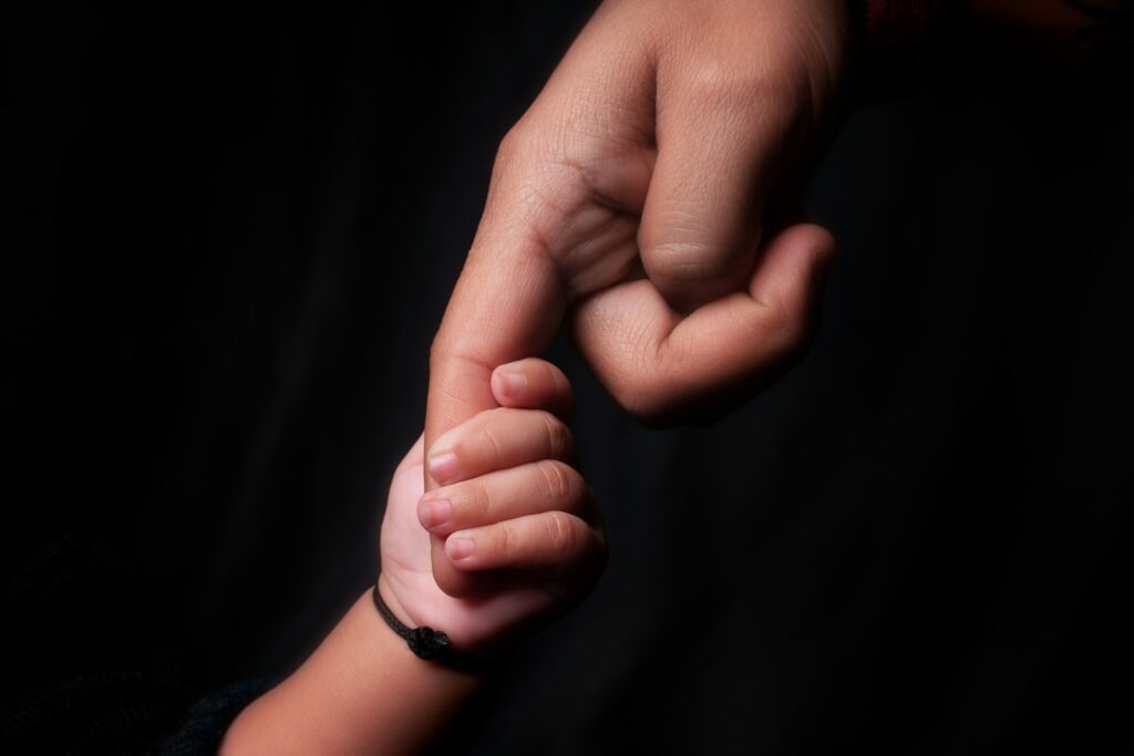 An adult holds a child's hand against a dark background