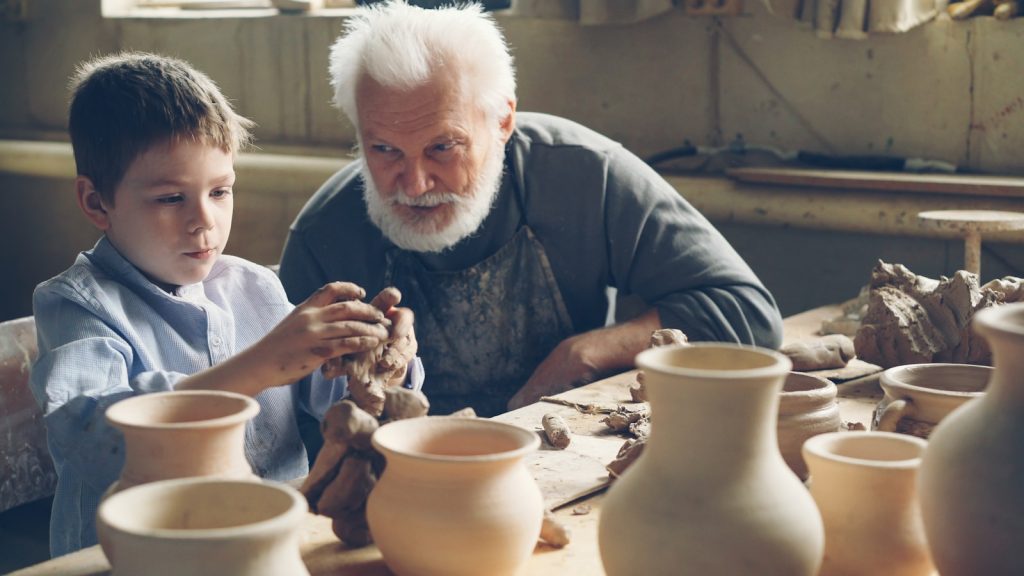 A grandfather teaches his grandson pottery.