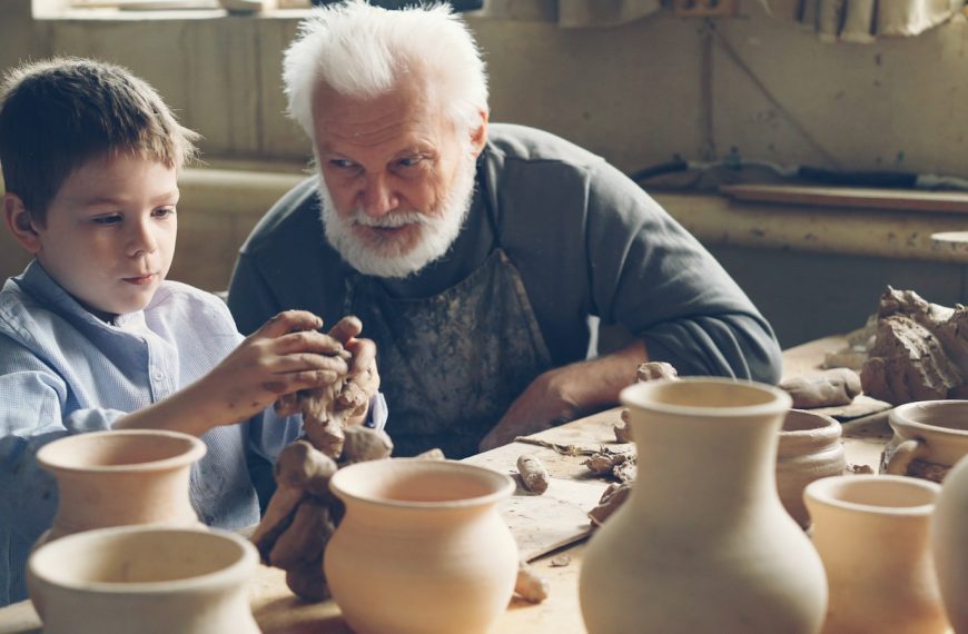 A grandfather teaches his grandson pottery.