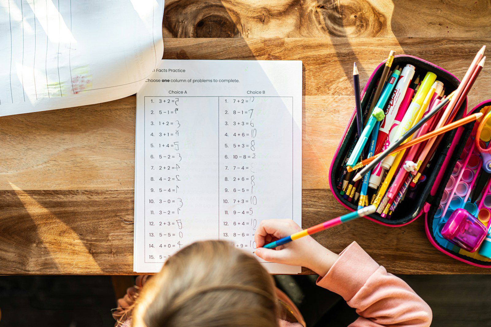 A little girl sitting at a table with a bag of pencils