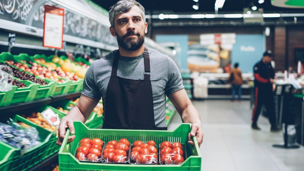 A grocery store worker holds a box of tomatoes.
