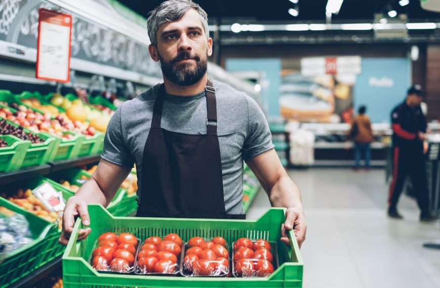 A grocery store worker holds a box of tomatoes.