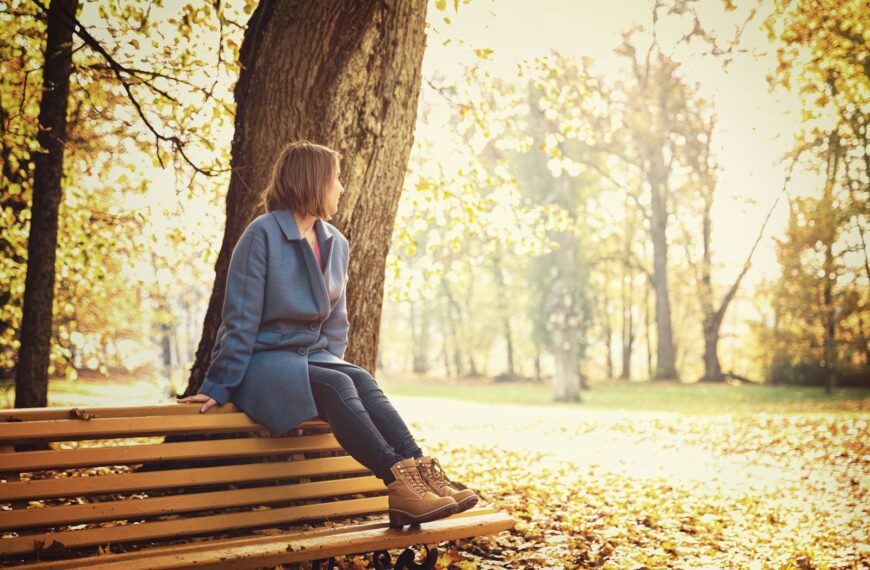 woman in blue blazer sitting on brown wooden bench during daytime