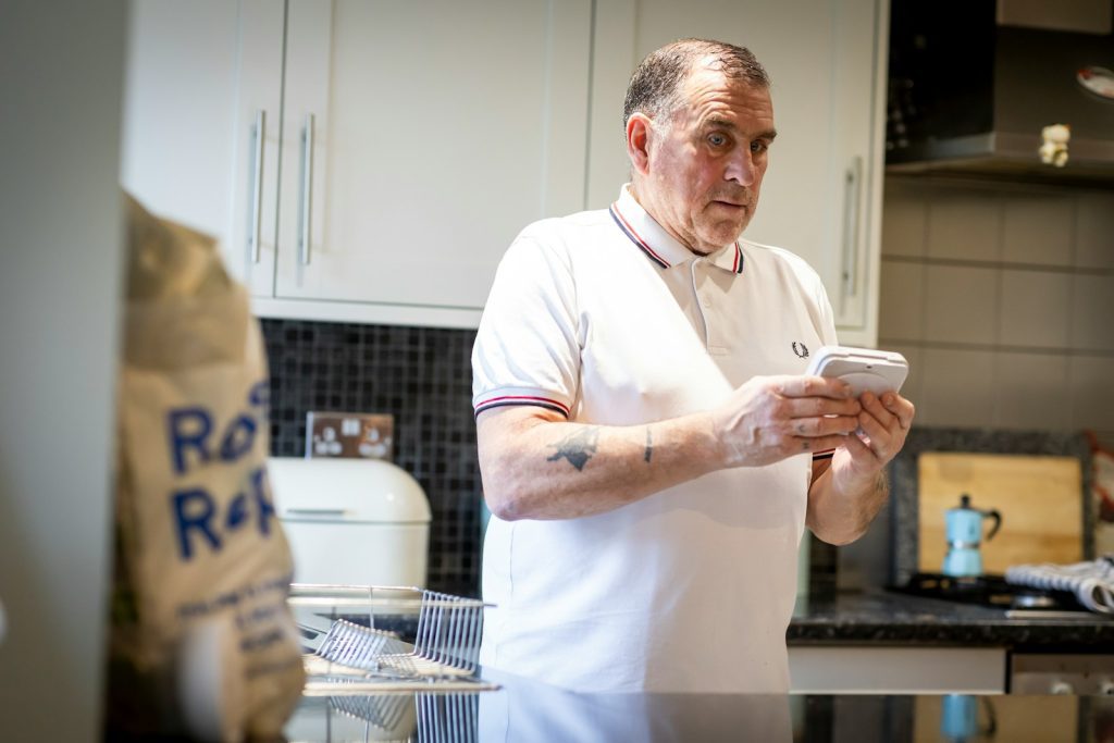 a man standing in a kitchen looking at a cell phone