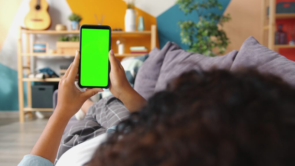 Person holding a smartphone with a green screen.