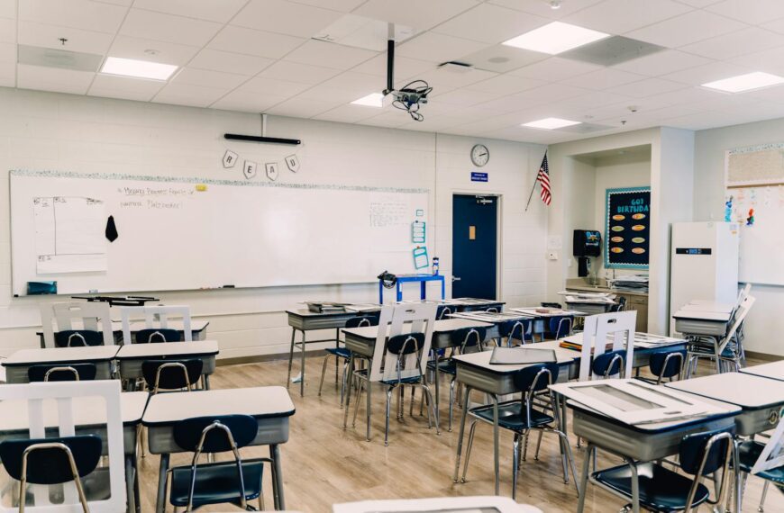 An empty classroom with arranged desks, whiteboard, and educational decor, ready for learning.