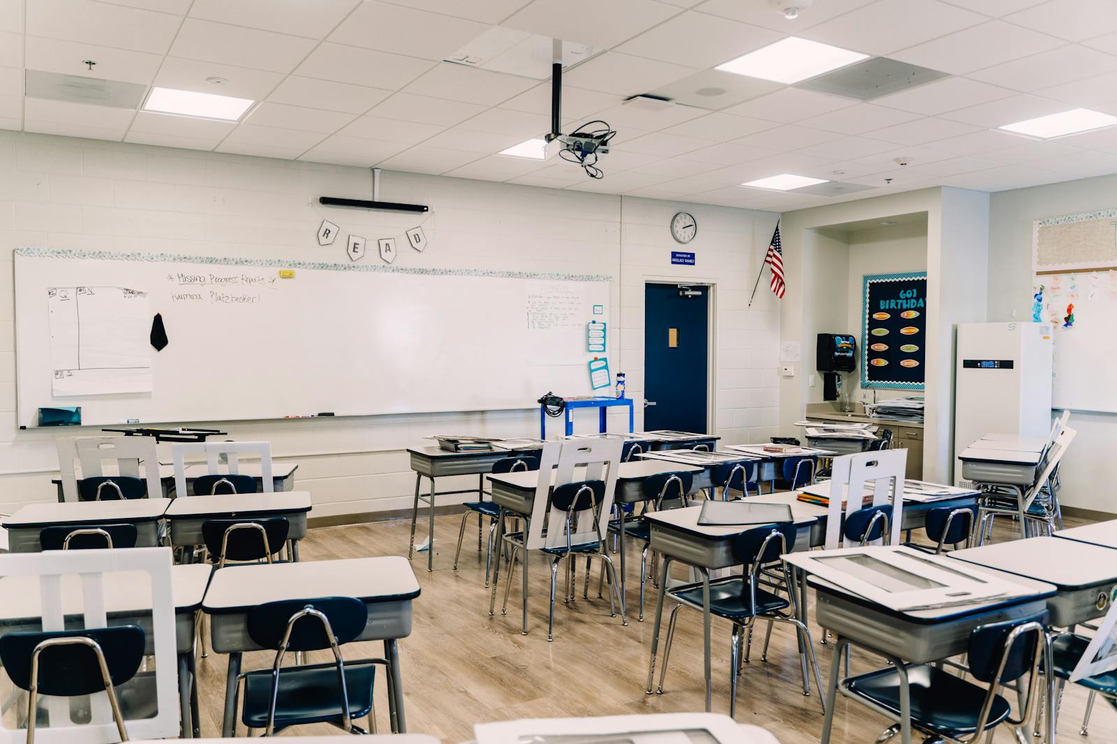 An empty classroom with arranged desks, whiteboard, and educational decor, ready for learning.