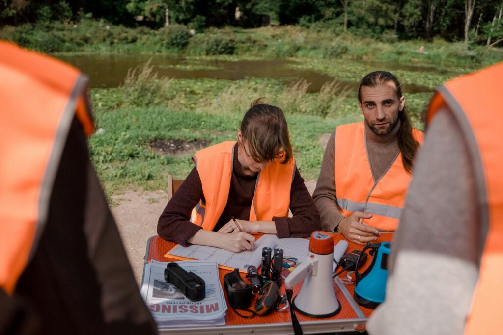 Volunteers in safety vests prepare for a search mission at a park near a water body.