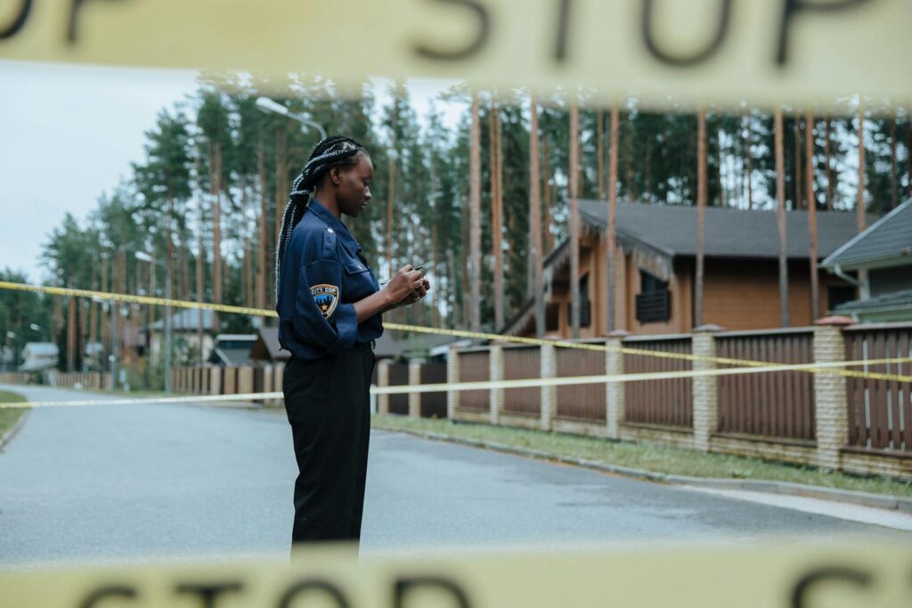 Police officer standing at a residential street crime scene with caution tape.