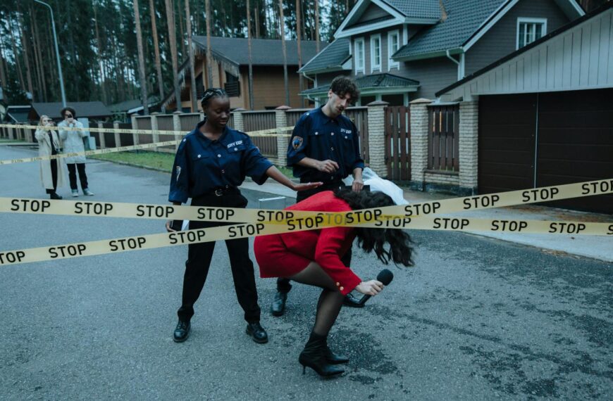 A reporter crosses caution tape at a police scene with officers nearby.