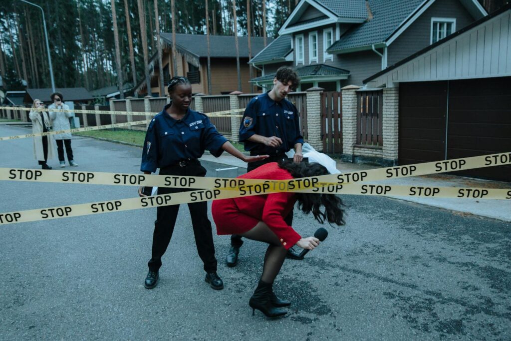 A reporter crosses caution tape at a police scene with officers nearby.