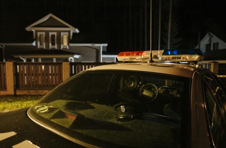 A parked police car at night in front of suburban houses with lights on, creating a dramatic mood.
