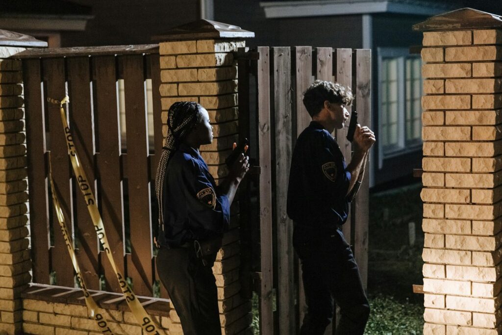 Two police officers investigate a crime scene at night, entering a house with caution.