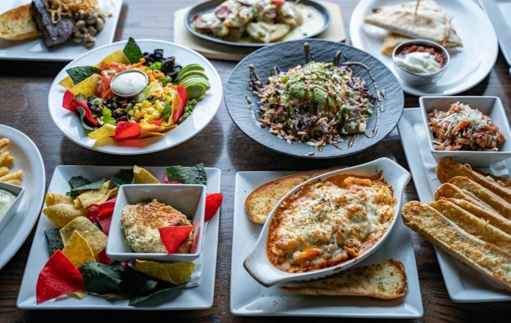 A colorful spread of various cuisines featuring salads, pasta, and appetizers on a restaurant table.