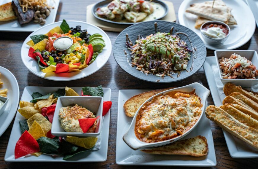 A colorful spread of various cuisines featuring salads, pasta, and appetizers on a restaurant table.