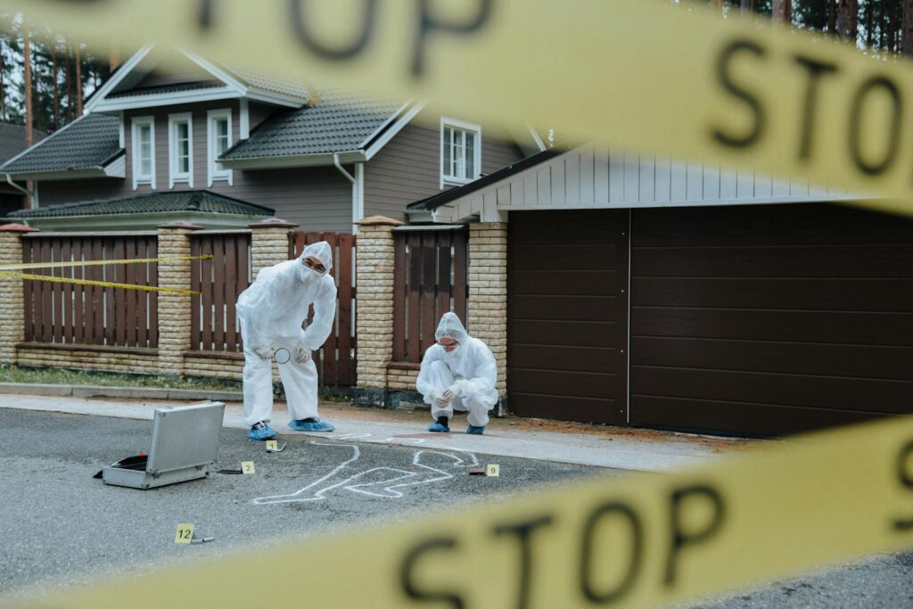 Forensic team examining crime scene with chalk outline and evidence markers outdoors.