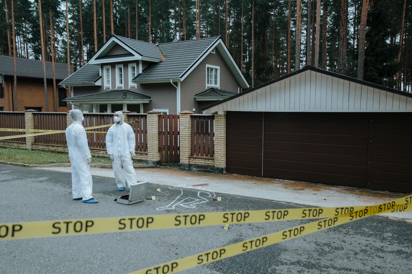 Crime scene investigators in protective suits examining evidence at a suburban house with yellow tape.