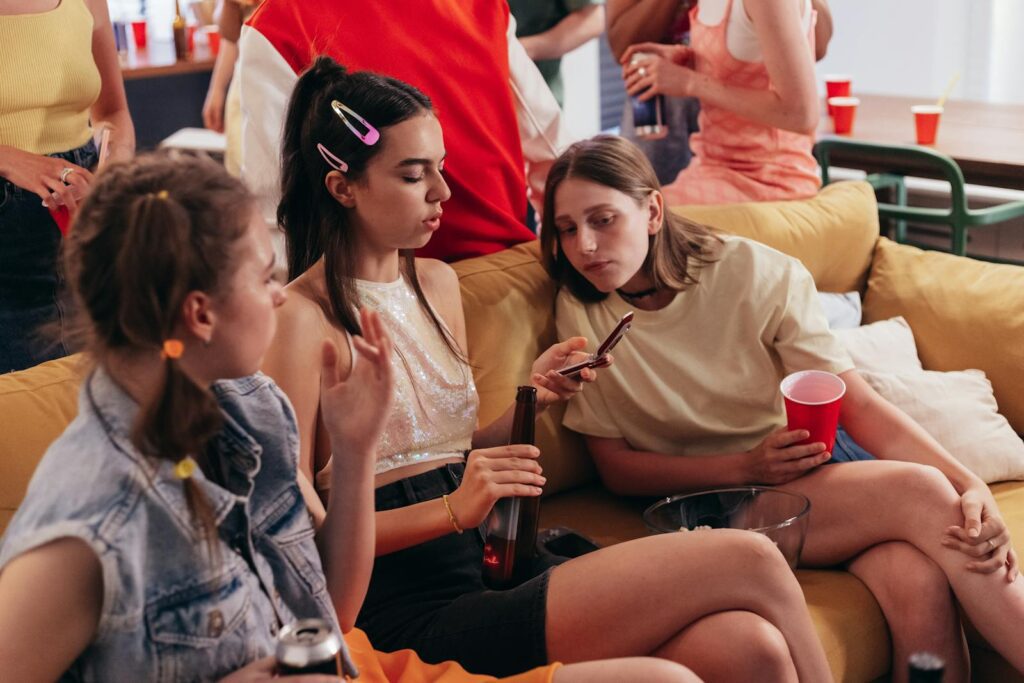 Young women at a casual house party chatting and using mobile phones.