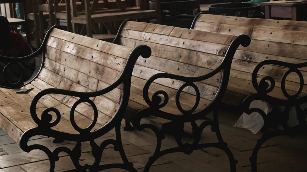 Wooden benches with decorative metal armrests arranged in an indoor workshop setting.