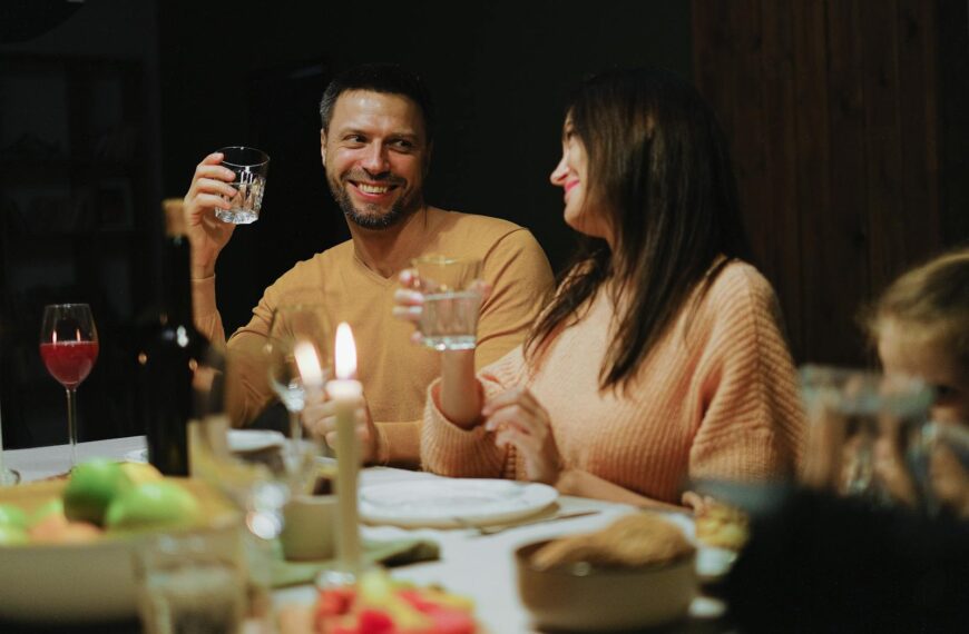 A smiling couple enjoying a romantic dinner at home, holding glasses and chatting warmly.