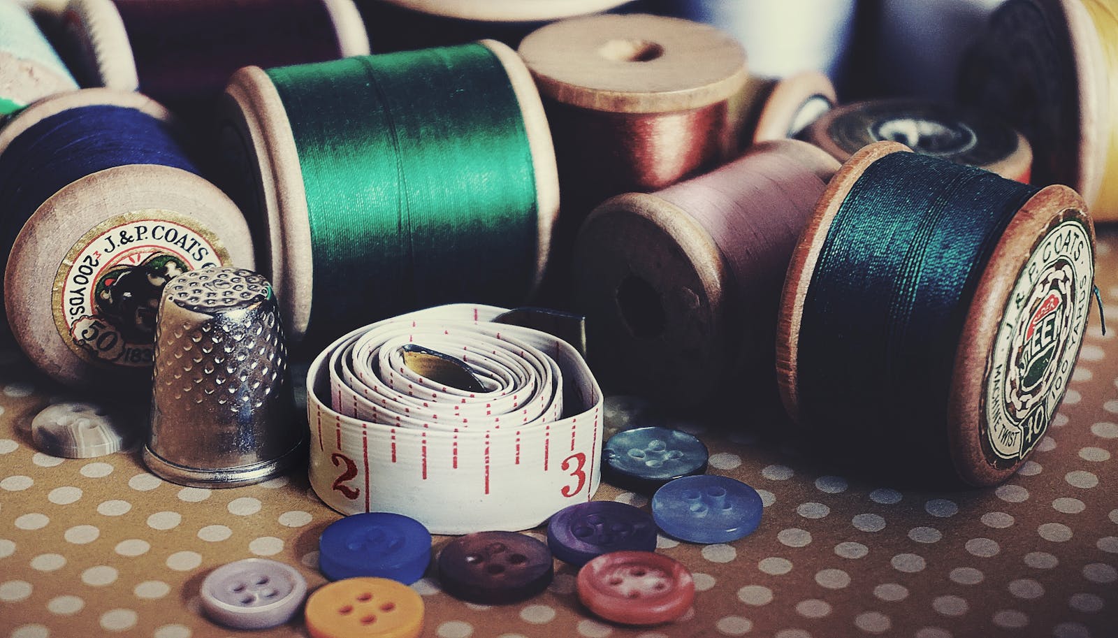 Close-up of vintage sewing essentials including threads, buttons, thimble, and measuring tape.