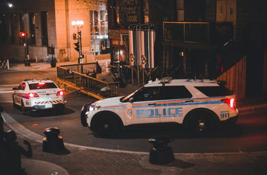 Two police cars patrolling a city street at night with warm lighting creating a dramatic urban mood.