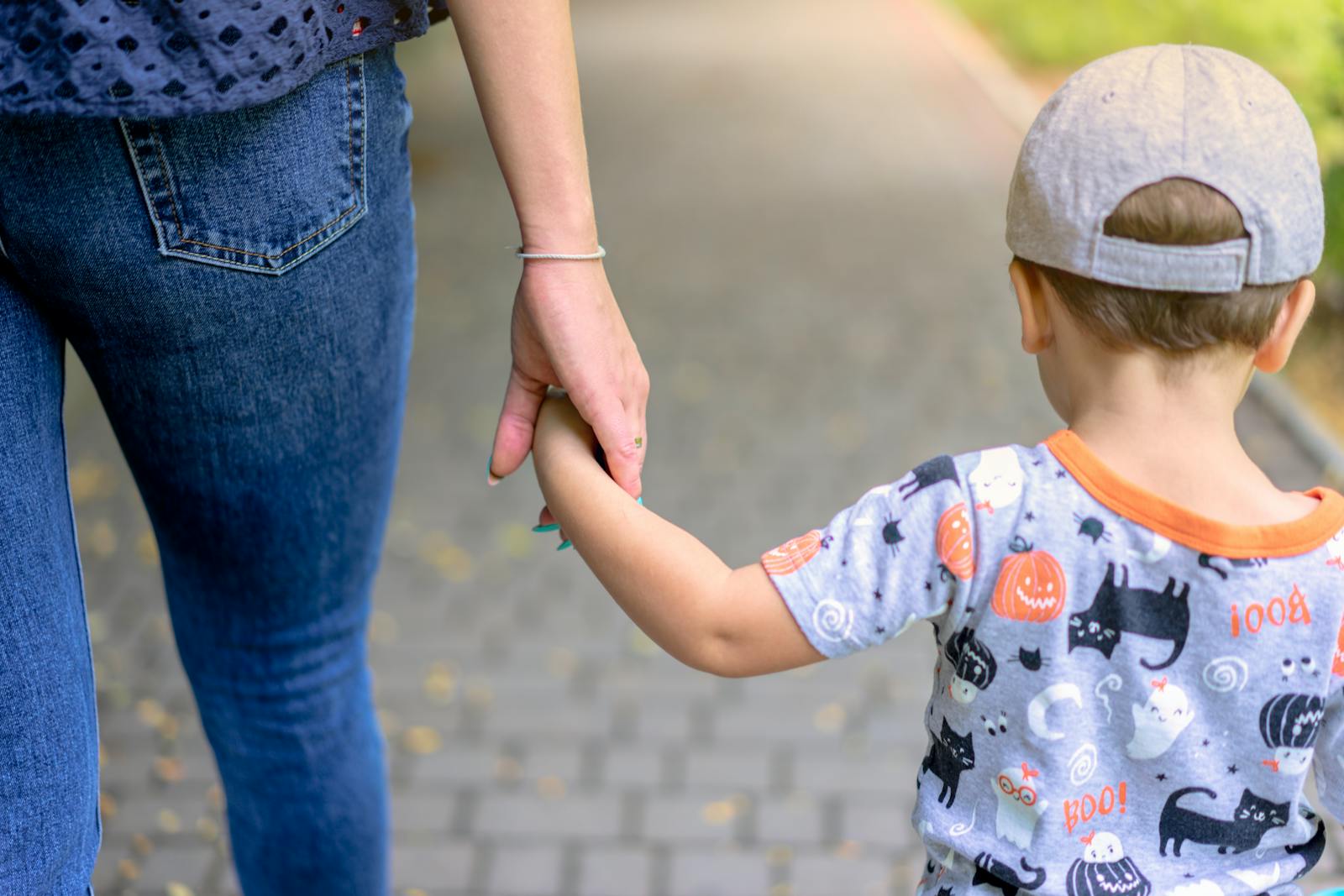 A mother and child enjoy a walk together holding hands on a sunny day.