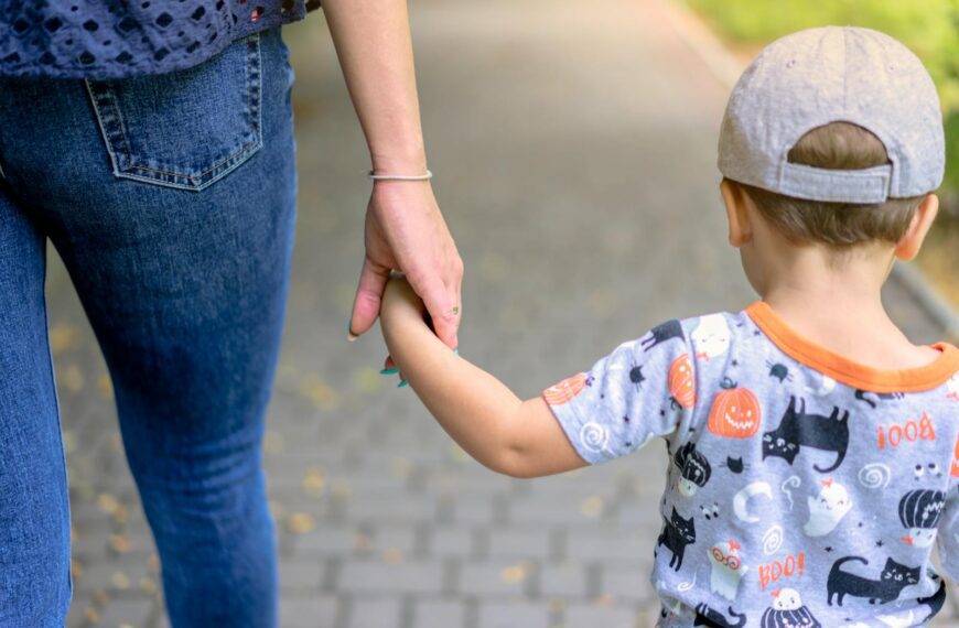 A mother and child enjoy a walk together holding hands on a sunny day.