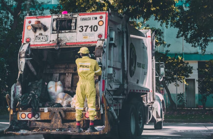 Sanitation worker collecting waste in Cali, Colombia. Urban scene with a garbage truck.