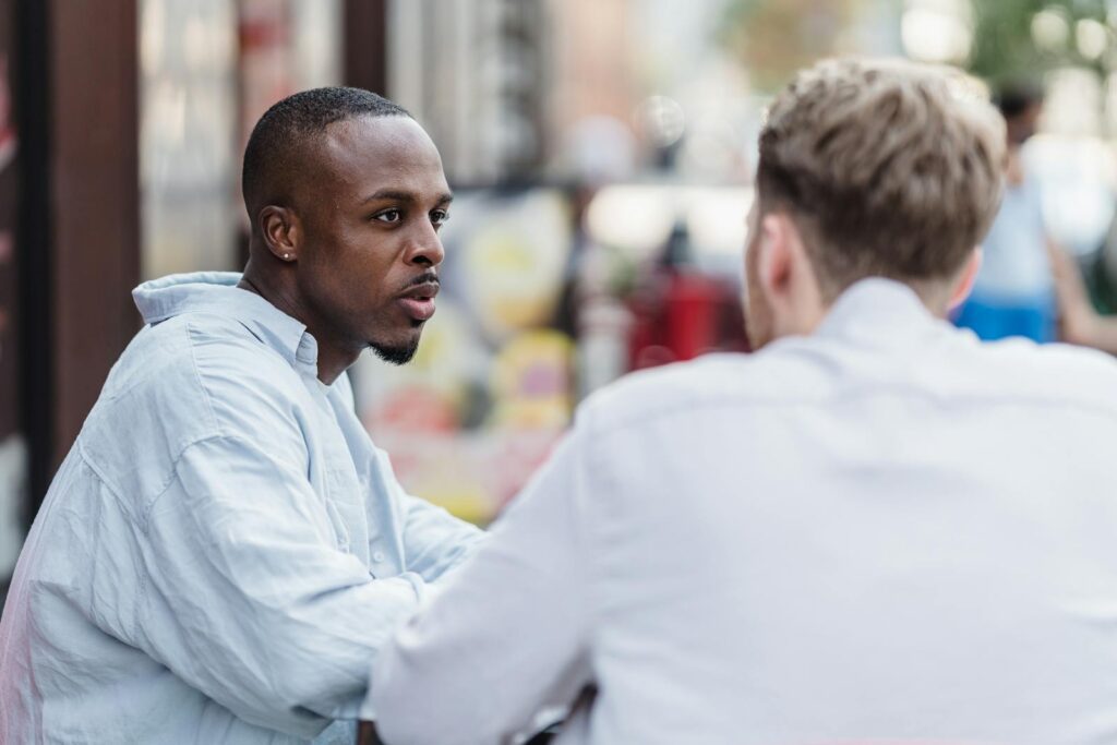 Two men having a conversation in an outdoor setting on a sunny day.