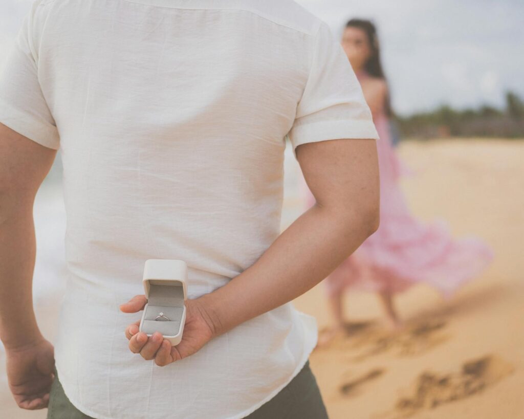 A man hides an engagement ring behind his back, preparing to propose on a beach in Phu Quoc.