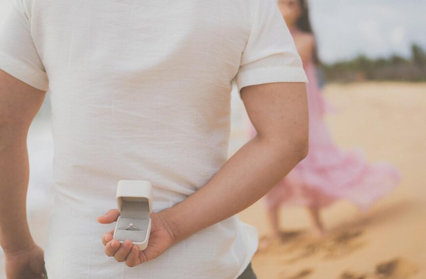 A man hides an engagement ring behind his back, preparing to propose on a beach in Phu Quoc.